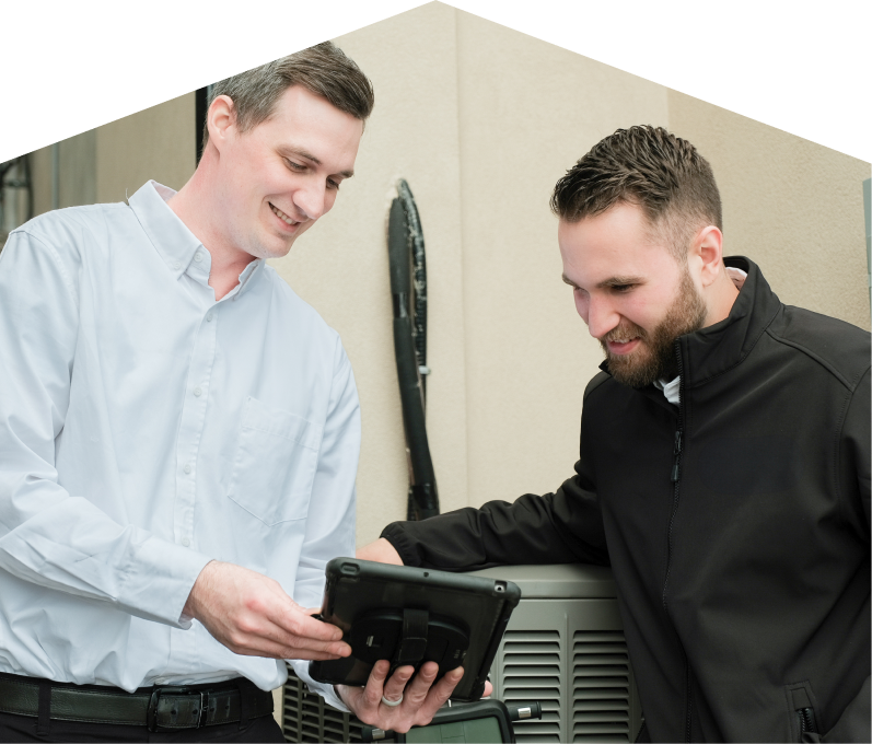 A M&K technician in a white shirt shows service details on a tablet to a smiling client in a black jacket, standing beside an AC unit outside a beige building. A M&K technician in a white shirt shows service details on a tablet to a smiling client in a black jacket, standing beside an AC unit outside a beige building.