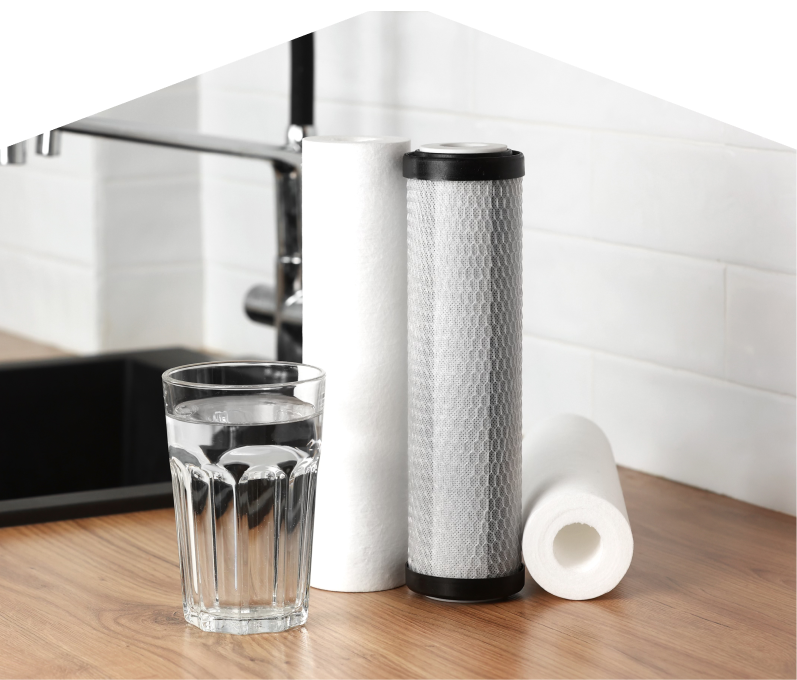 Set of M&K water filtration cartridges placed beside a clear glass of water on a kitchen countertop, with a sink and modern faucet in the background. Set of M&K water filtration cartridges placed beside a clear glass of water on a kitchen countertop, with a sink and modern faucet in the background.