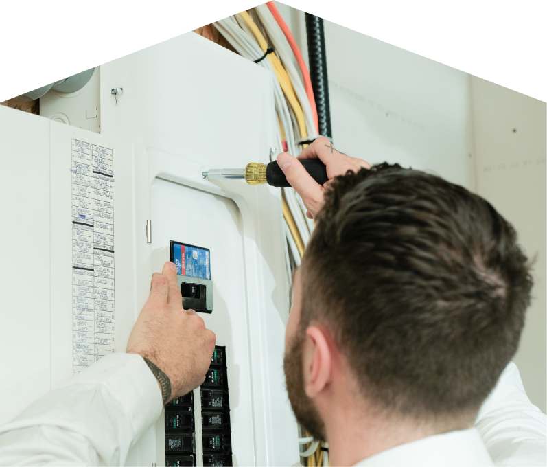 M&K electrician using a screwdriver to perform an electrical panel upgrade, working near organized wiring in a residential wall. M&K electrician using a screwdriver to perform an electrical panel upgrade, working near organized wiring in a residential wall.