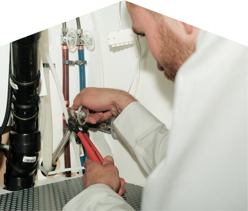 M&K plumbing expert tightening connections under a sink during a faucet installation, surrounded by hot and cold water supply lines and PVC drainage. M&K plumbing expert tightening connections under a sink during a faucet installation, surrounded by hot and cold water supply lines and PVC drainage.