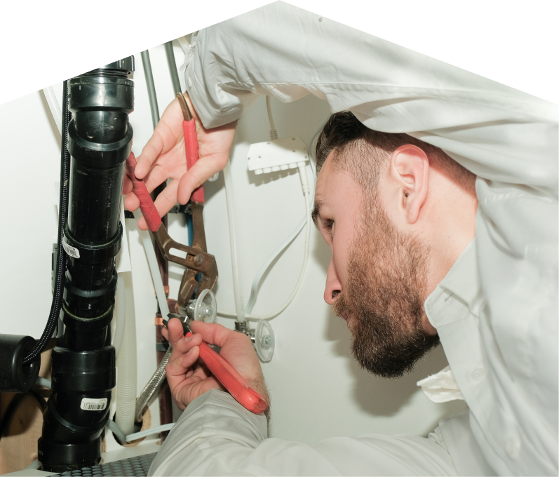 M&K plumbing specialist uses hand tools to tighten pipe fittings beneath a sink during a repair, with visible wiring and drainage lines in the background. M&K plumbing specialist uses hand tools to tighten pipe fittings beneath a sink during a repair, with visible wiring and drainage lines in the background.