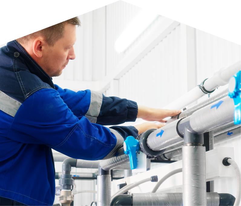 M&K water damage and restoration specialist in a blue uniform adjusts insulated piping on a water system inside a bright utility room.