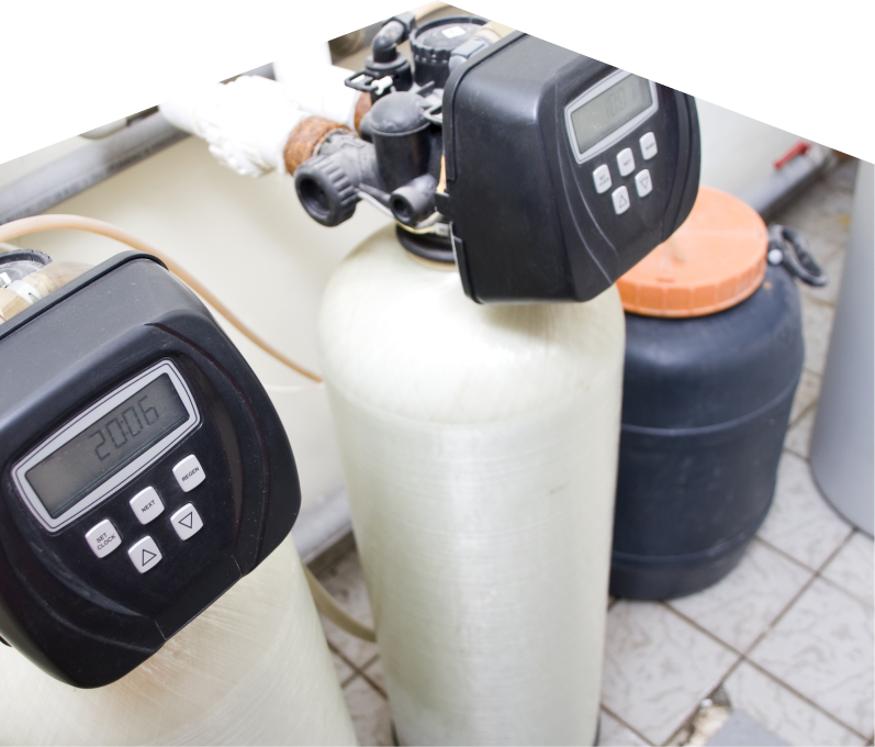 M&K water softener installation showing dual resin tanks with digital control heads and a brine tank in a tiled utility area. M&K water softener installation showing dual resin tanks with digital control heads and a brine tank in a tiled utility area.