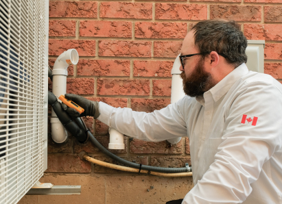 A M&K HVAC specialist wearing glasses and gloves uses a diagnostic tool to service an outdoor AC unit beside a brick wall. A M&K HVAC specialist wearing glasses and gloves uses a diagnostic tool to service an outdoor AC unit beside a brick wall.