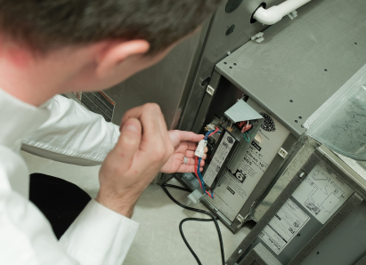 A M&K heating technician inspecting internal wiring during a service check on a residential heating unit. A M&K heating technician inspecting internal wiring during a service check on a residential heating unit.
