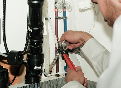 Using two pipe wrenches, a M&K professional plumber services a pipe connection near a vertical flue or vent pipe. Using two pipe wrenches, a M&K professional plumber services a pipe connection near a vertical flue or vent pipe.